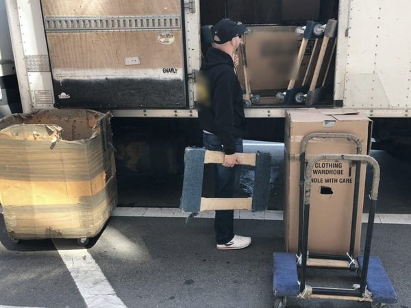 One of our movers unloading padded furniture next to wardrobe boxes on a dolly at the truck