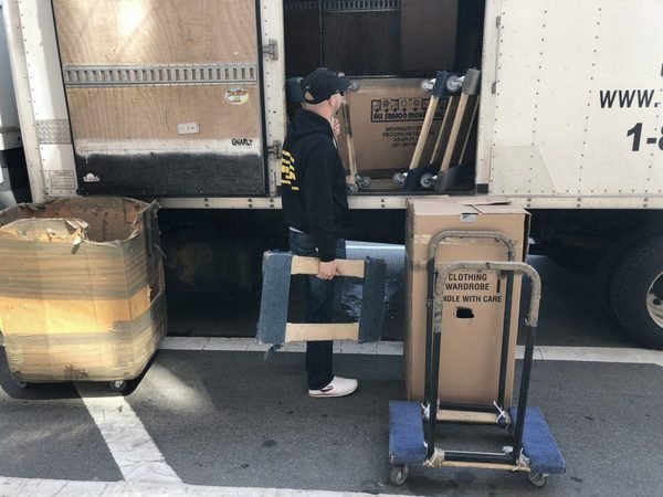 One of our movers unloading padded furniture next to wardrobe boxes on a dolly at the truck