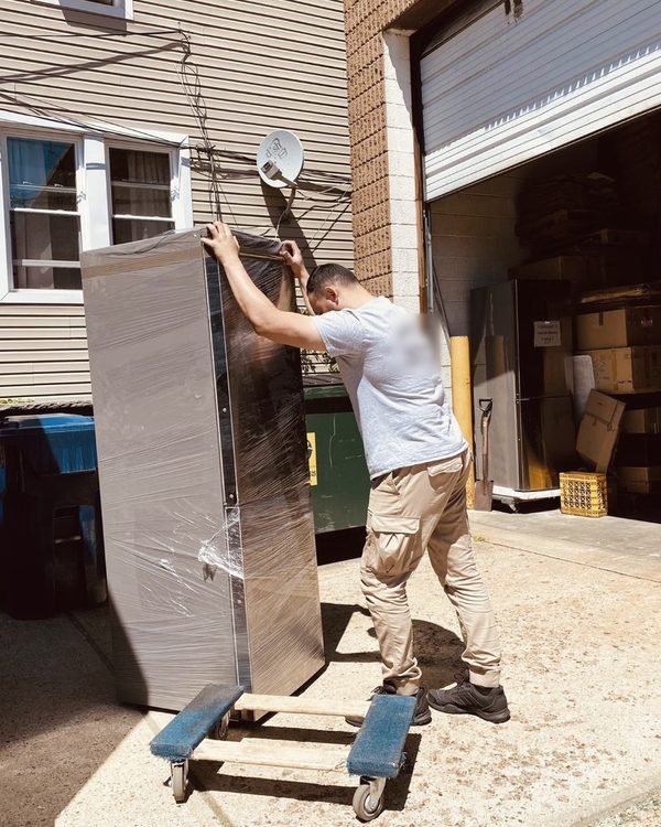 One of our movers steadying a tall stretch-wrapped cabinet on a dolly